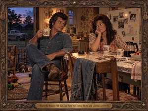 In a cozy 1970s country kitchen, a denim-clad man and floral-dressed woman trade teasing glances over coffee. Childrens toys, family photographs, and a resting hound suggest lived-in affection. Golden lamplight warms faded wallpaper against cool twilight outside, while cinematic realism, an ornate carved wooden frame, and brass title plate evoke nostalgic humor.
